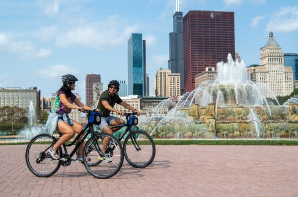 Two people riding bicycles past fountain